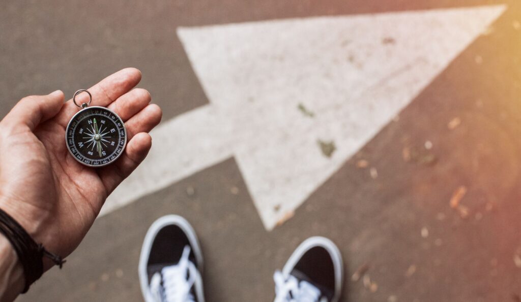 Person holding a compass, standing at a crossroads with a bold white arrow — symbolising direction and strategy for getting found online.